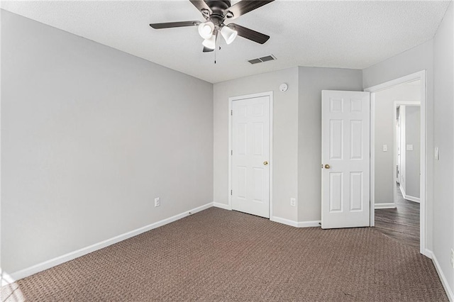 unfurnished bedroom featuring visible vents, baseboards, dark carpet, a textured ceiling, and a ceiling fan