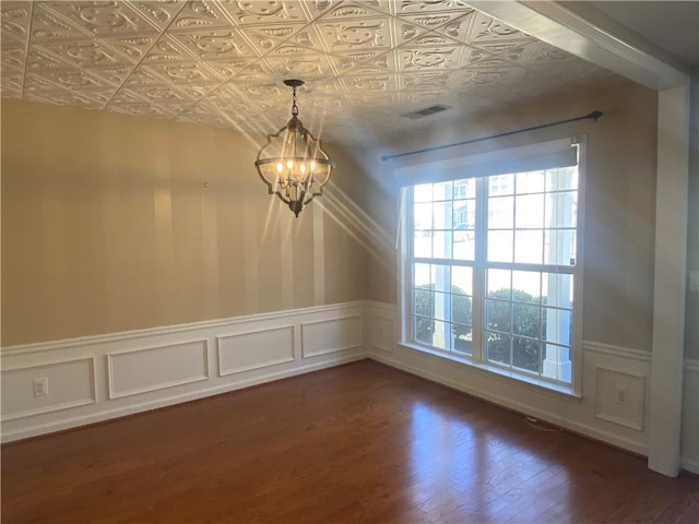 unfurnished dining area with visible vents, a wainscoted wall, a notable chandelier, an ornate ceiling, and dark wood-style flooring