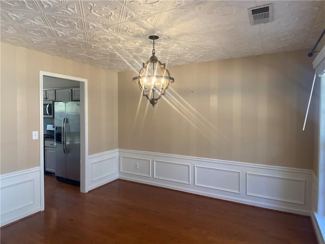 unfurnished dining area featuring visible vents, a wainscoted wall, an ornate ceiling, dark wood-style floors, and a chandelier