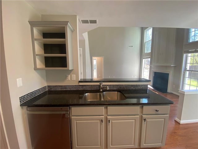 kitchen featuring visible vents, a sink, a peninsula, a fireplace, and dishwasher