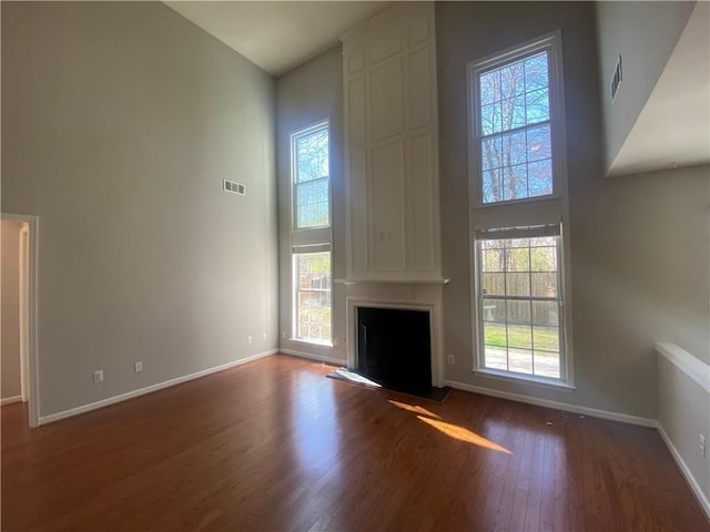 unfurnished living room featuring visible vents, wood finished floors, a high ceiling, a fireplace, and baseboards