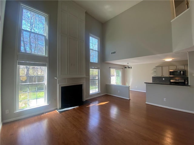 unfurnished living room with dark wood-style floors, baseboards, visible vents, a high ceiling, and a large fireplace