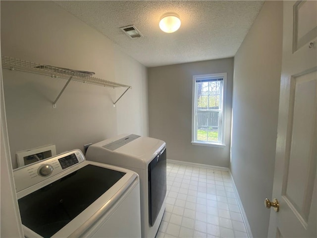 clothes washing area featuring visible vents, a textured ceiling, separate washer and dryer, baseboards, and laundry area