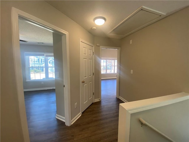 hall featuring dark wood finished floors, an upstairs landing, a textured ceiling, and baseboards