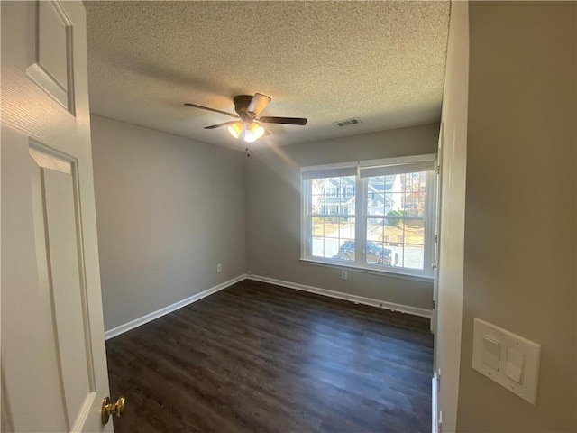 unfurnished room featuring dark wood-style floors, visible vents, baseboards, and a ceiling fan