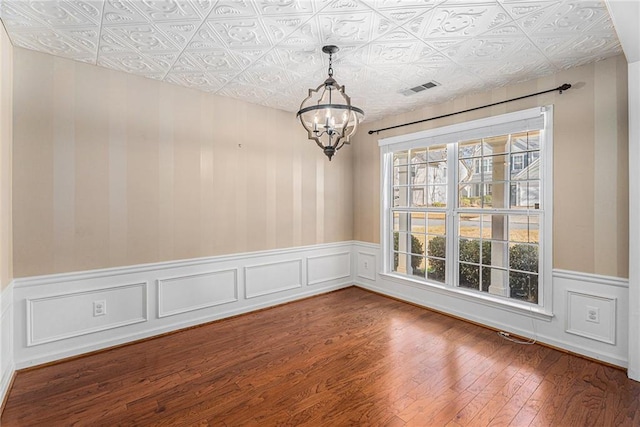 unfurnished room with visible vents, a wainscoted wall, an ornate ceiling, dark wood finished floors, and an inviting chandelier