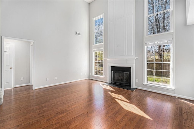 unfurnished living room featuring visible vents, baseboards, hardwood / wood-style floors, a fireplace, and a high ceiling