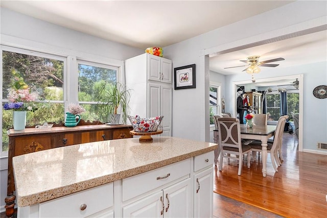 kitchen with light stone counters, ceiling fan, white cabinetry, a center island, and light wood-type flooring