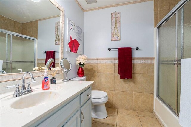 full bathroom featuring toilet, combined bath / shower with glass door, tile patterned flooring, tile walls, and vanity