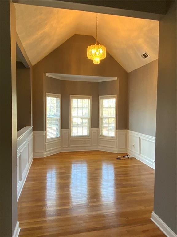 spare room featuring hardwood / wood-style floors, an inviting chandelier, and lofted ceiling