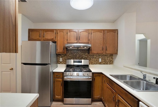 kitchen featuring sink, appliances with stainless steel finishes, backsplash, light hardwood / wood-style floors, and a textured ceiling