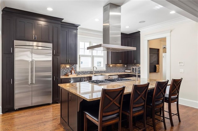 kitchen featuring a kitchen island, appliances with stainless steel finishes, island range hood, a kitchen bar, and light stone countertops