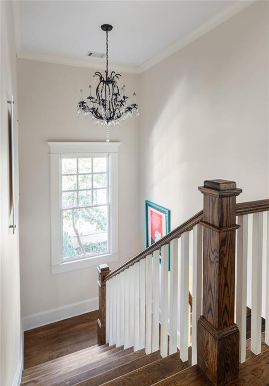 stairway with a notable chandelier, crown molding, and wood-type flooring