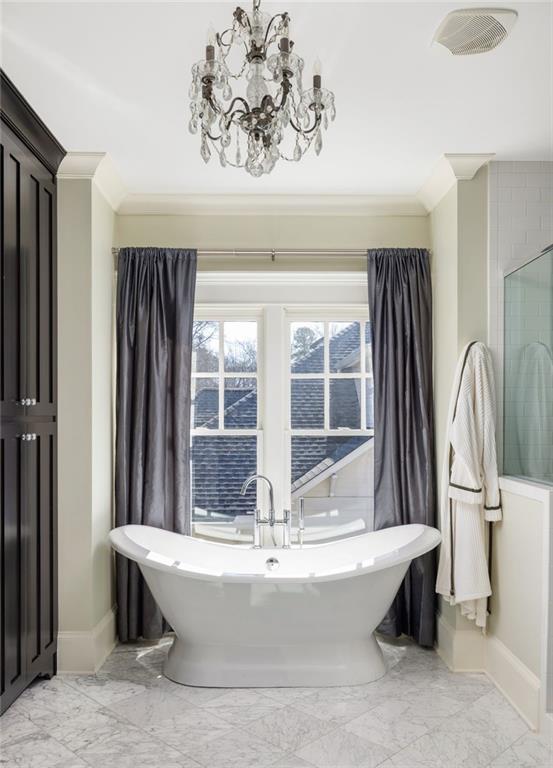 bathroom with crown molding, an inviting chandelier, and a bathtub