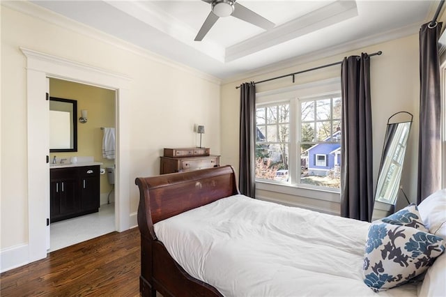 bedroom with dark hardwood / wood-style floors, connected bathroom, sink, a tray ceiling, and crown molding