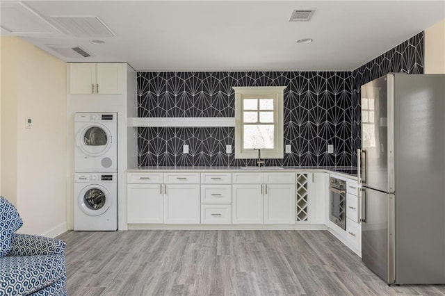 kitchen featuring sink, light hardwood / wood-style flooring, stainless steel appliances, stacked washer / dryer, and white cabinets