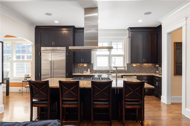 kitchen with a breakfast bar area, a center island, appliances with stainless steel finishes, island exhaust hood, and light stone countertops