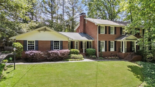 colonial home featuring brick siding, a chimney, and a front yard