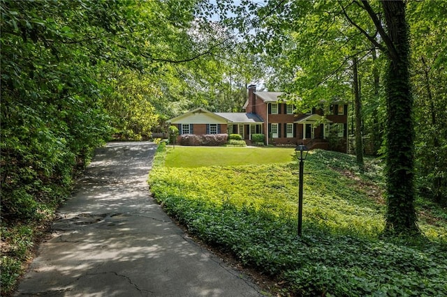 view of front facade featuring asphalt driveway, a front lawn, and a chimney