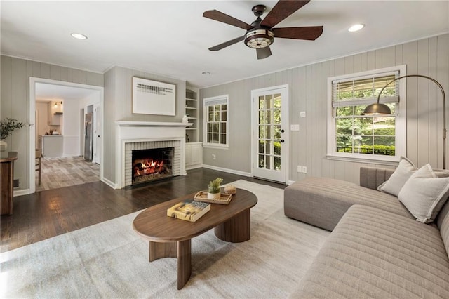 living area featuring wood finished floors, crown molding, a ceiling fan, a brick fireplace, and recessed lighting