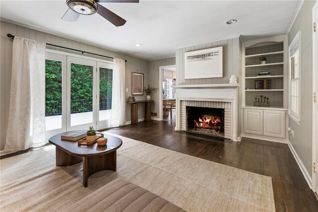 living area with wood finished floors, ornamental molding, a ceiling fan, a fireplace, and baseboards