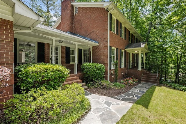doorway to property with brick siding, covered porch, a chimney, and a yard