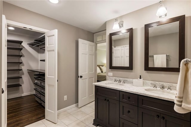 full bathroom with double vanity, a walk in closet, baseboards, and tile patterned flooring