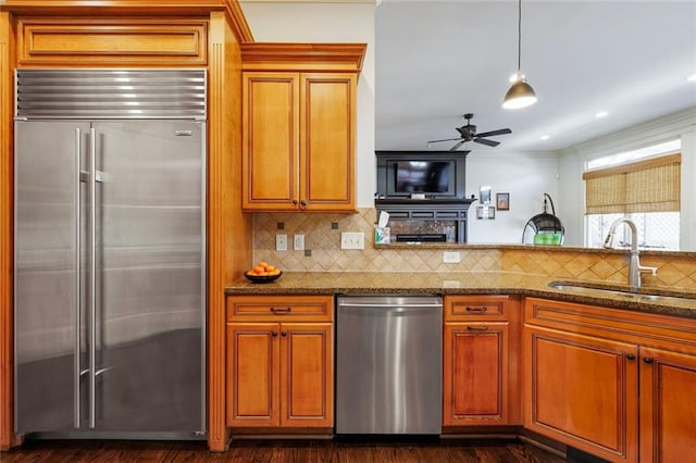 kitchen with appliances with stainless steel finishes, dark stone counters, a sink, and backsplash