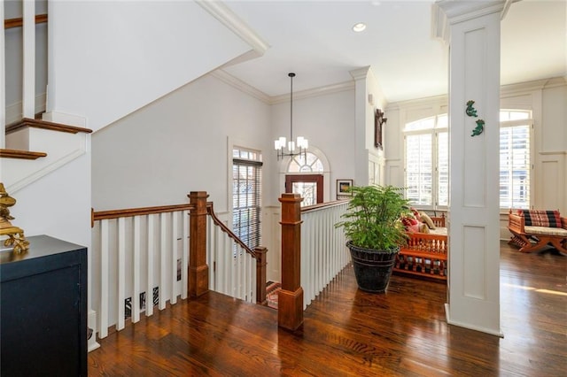 stairway with an inviting chandelier, wood finished floors, decorative columns, and crown molding