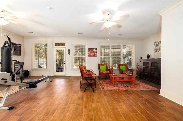 living area featuring a ceiling fan, wood finished floors, visible vents, and crown molding