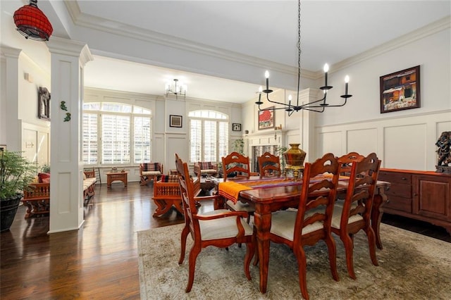 dining area with dark wood-style flooring, a fireplace, decorative columns, a decorative wall, and ornamental molding