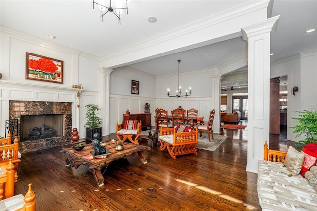 living room featuring ornate columns, an inviting chandelier, a high end fireplace, and a decorative wall