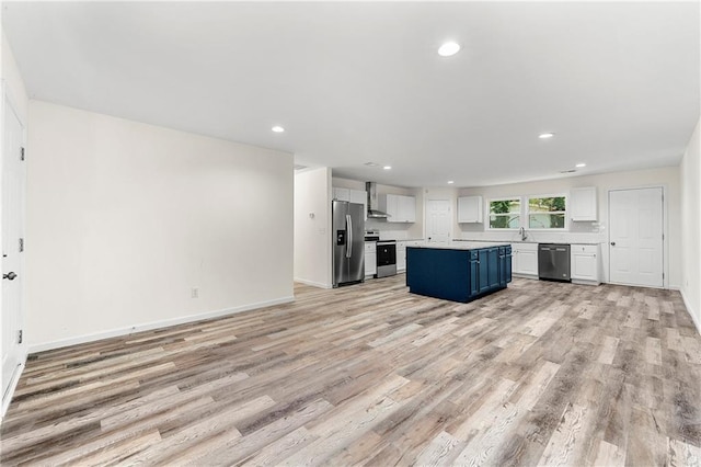 kitchen with light wood-type flooring, wall chimney exhaust hood, stainless steel appliances, blue cabinetry, and a kitchen island