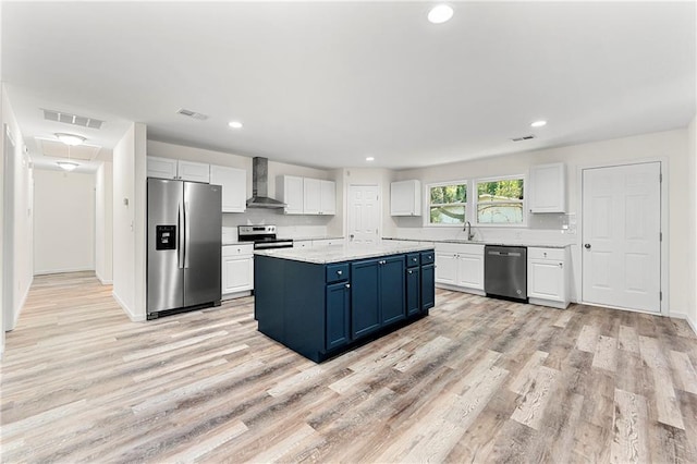 kitchen featuring wall chimney exhaust hood, stainless steel appliances, blue cabinetry, white cabinetry, and a kitchen island