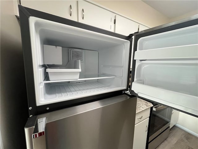 interior details with white cabinetry, light countertops, wood finished floors, and refrigerator