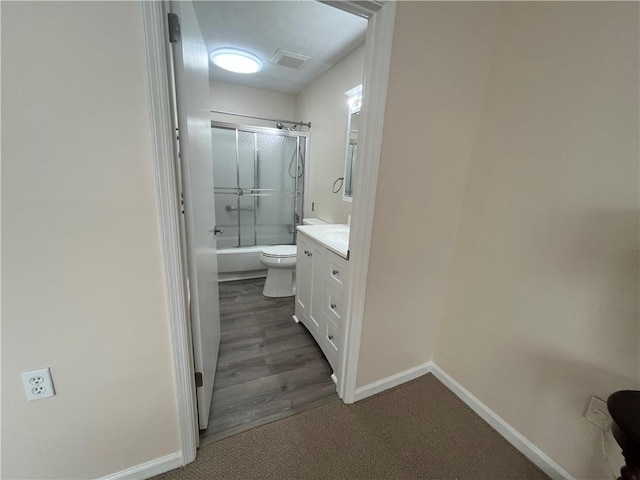 bathroom with visible vents, toilet, enclosed tub / shower combo, vanity, and baseboards