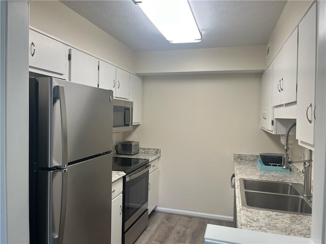 kitchen with stainless steel appliances, light countertops, a sink, a textured ceiling, and wood finished floors