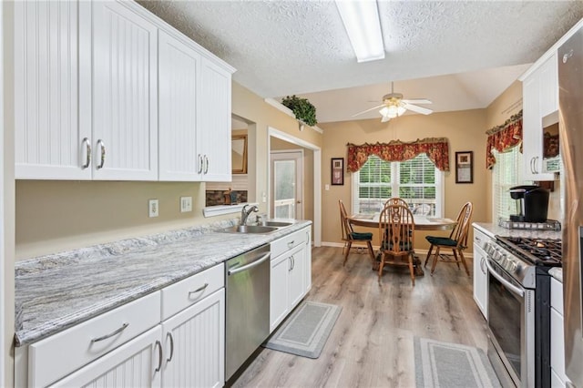 kitchen with ceiling fan, white cabinets, a sink, light wood finished floors, and appliances with stainless steel finishes
