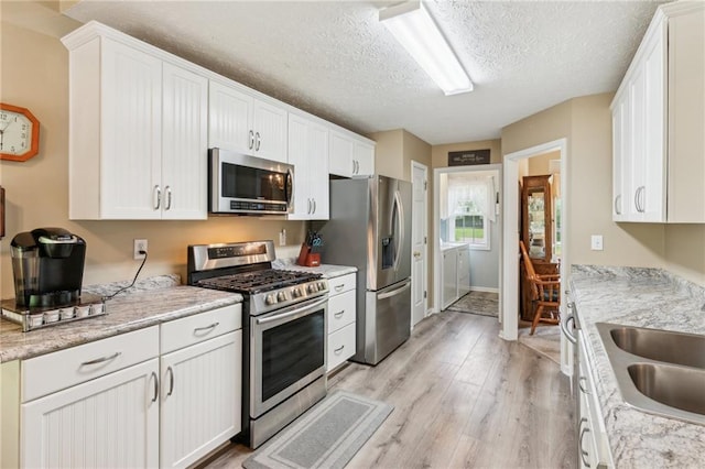 kitchen with a sink, light wood-style flooring, appliances with stainless steel finishes, and white cabinets