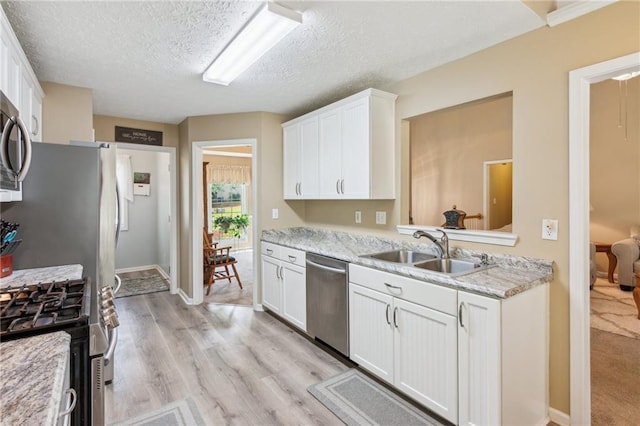 kitchen featuring white cabinets, appliances with stainless steel finishes, a sink, and light wood-style floors