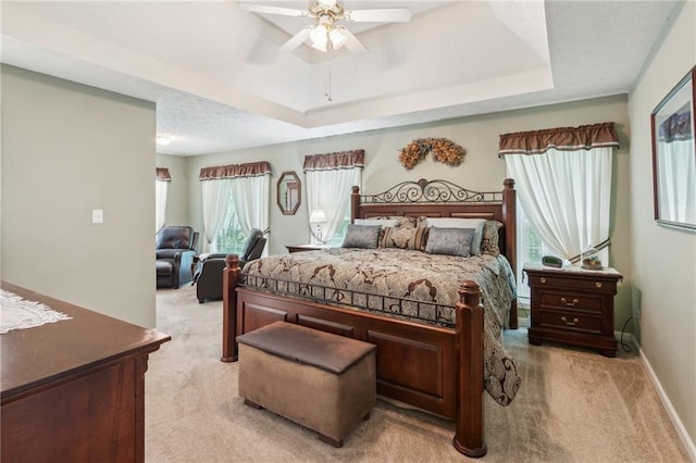 bedroom with baseboards, light carpet, ceiling fan, and a raised ceiling