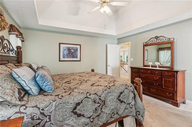 bedroom with a raised ceiling, light carpet, and a ceiling fan