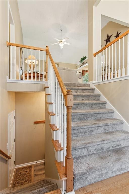 stairway with baseboards, a ceiling fan, a towering ceiling, and wood finished floors