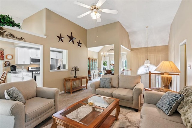 living area with high vaulted ceiling, baseboards, light carpet, and ceiling fan with notable chandelier