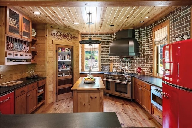 kitchen with a center island, wall chimney exhaust hood, light hardwood / wood-style floors, and appliances with stainless steel finishes