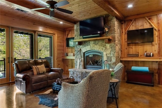 living room with wooden walls, concrete floors, a stone fireplace, wood ceiling, and ceiling fan