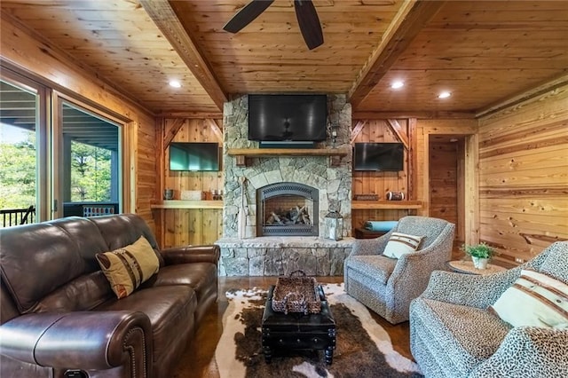 living room with a stone fireplace, ceiling fan, beamed ceiling, wooden walls, and wooden ceiling