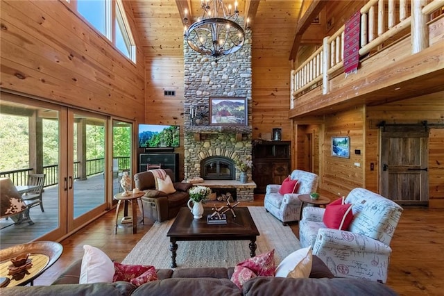 living room featuring a fireplace, an inviting chandelier, wood-type flooring, wood walls, and high vaulted ceiling