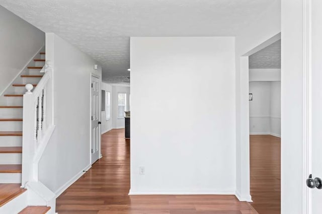 hallway featuring stairway, a textured ceiling, baseboards, and wood finished floors