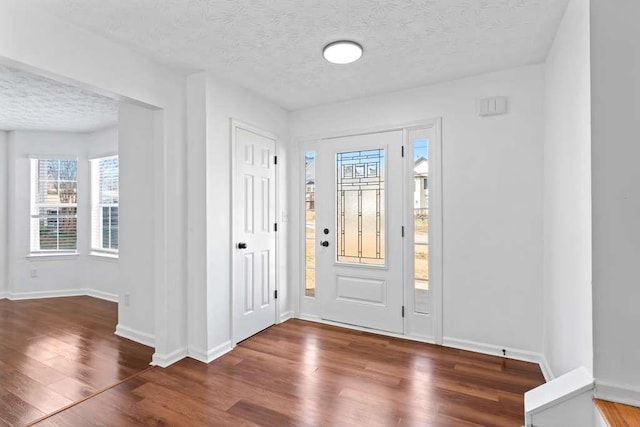 foyer entrance with baseboards, a textured ceiling, and wood finished floors